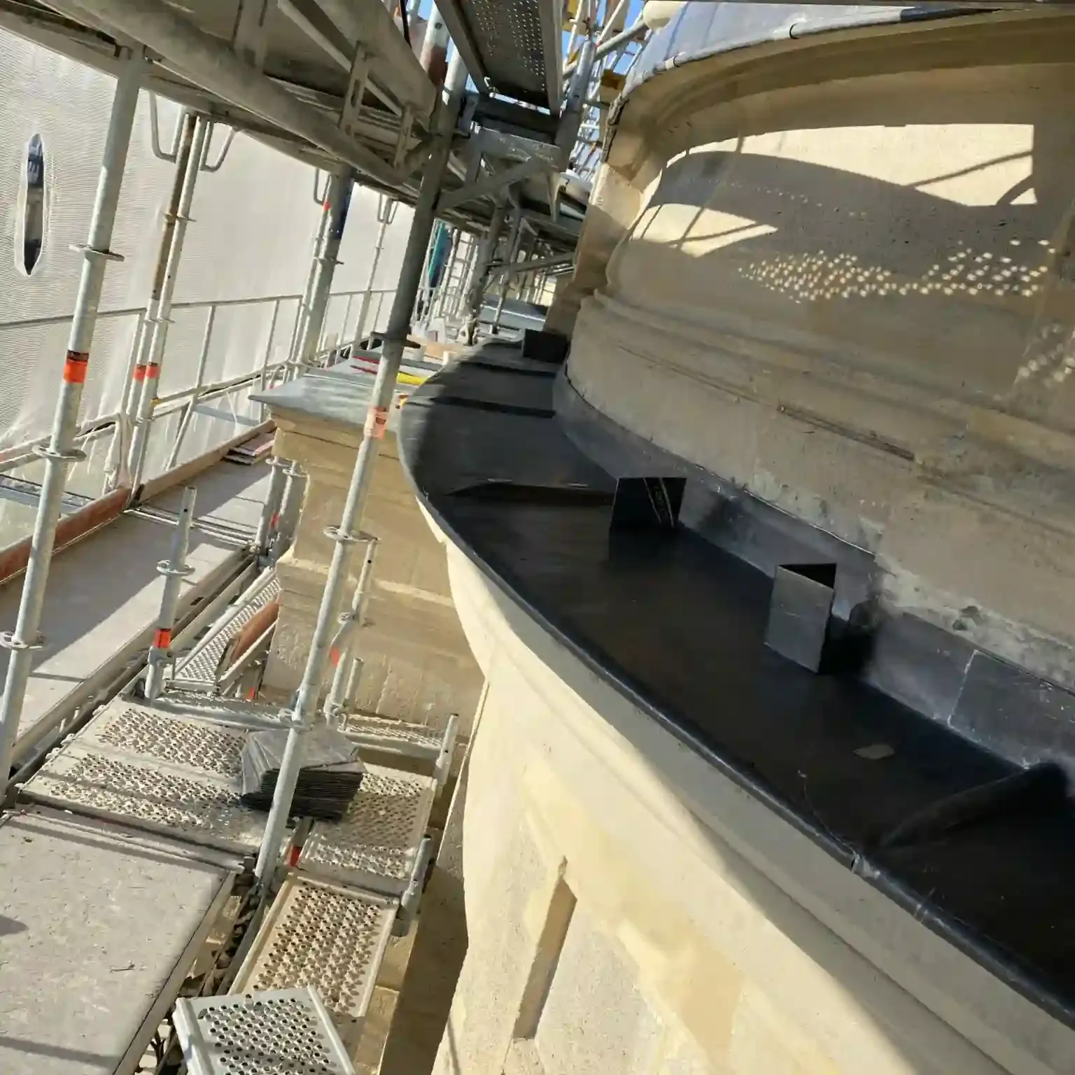 Corniche arrondie en pierre protégée par une bande métallique, chantier sous échafaudage